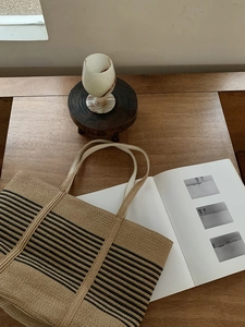 Detail of woven straw tote bag with black stripes on a wooden surface with lifestyle props