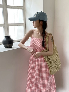 Gros plan d'un sac cabas en paille kaki avec une robe à carreaux vichy rose