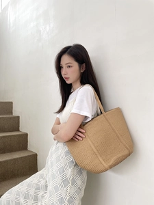 Detail of a khaki woven straw tote bag with fine texture on a female model