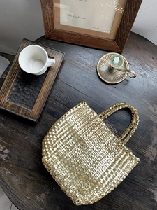 Close-up of golden woven handbag with champagne metallic texture on a vintage wood desk