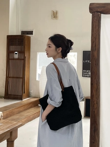 Close-up of black woven tote bag with brown leather straps worn by a model in a cafe