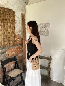 Detail of hand-woven hollow straw bag with slim strap on a model for a summer resort look
