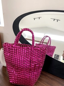 Close-up of a hot pink woven tote bag with metallic finish on a dark wooden table