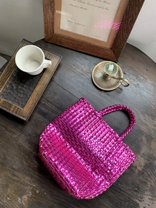 Detail of fuchsia woven tote bag with glossy finish and cross-weave texture on wood table