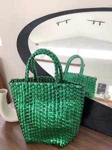 Detail of emerald green woven basket bag with metallic finish and textured handles