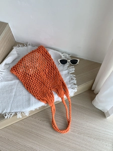 Close-up of bright orange handmade woven tote bag with sunglasses on a rustic setting