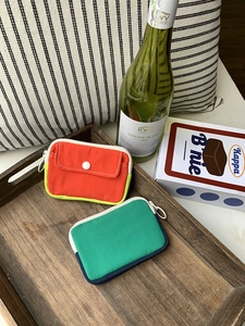 Mini canvas zipper coin purse and earphone pouch in red and green on a wooden tray