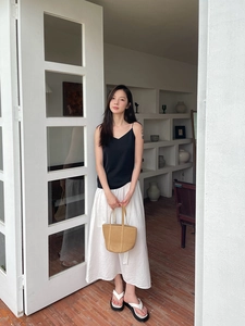 Detail of straw woven handbag paired with a black V-neck camisole and white midi skirt
