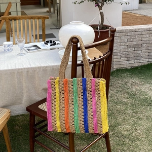 Colorful handmade woven straw tote bag with striped pattern hanging on a wooden chair
