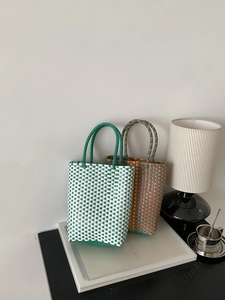 Detail of colorful PVC woven tote bags in green and orange checkers on a stylish desk