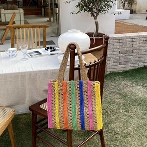 Large colorful striped straw tote bag hanging on a chair in a sunny outdoor cafe