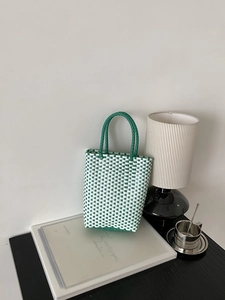 Detail of green and white checkered woven tote bag placed on a decorative book