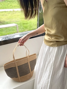 Detail of hand-woven straw tote bag with black stripes and sturdy top handles
