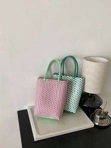 Detail view of pink and green woven PVC tote bags in a stylish home interior setting