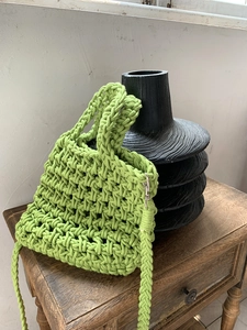 Detail of hand-woven grass green tote bag with silver metal hooks on wooden cabinet