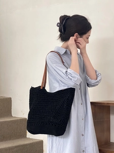 Black hollow woven tote bag with brown leather handles worn by a model in a cozy room
