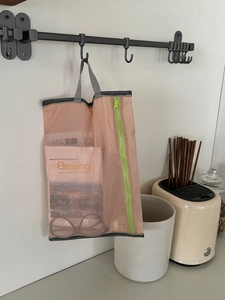 Pink mesh storage bag with green zipper and gray handle hanging in a home setting