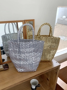 Chic metallic woven basket tote bag in silver and gold displayed on a wooden shelf