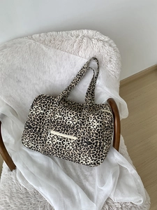 Detail of leopard print canvas tote bag with metal zipper and wide handles on white chair