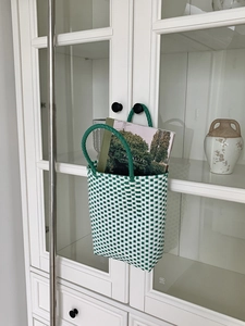Detail of green and white woven PVC tote bag hanging on white cabinet with magazine