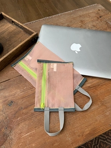 Detail of pink mesh storage bags with green zippers and grey handles on wooden desk