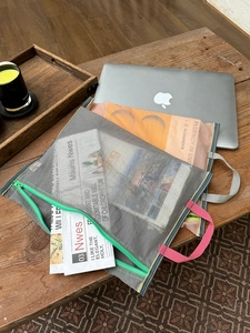 Detail showing the grey mesh file bag with green zipper and pink handle on a wooden desk