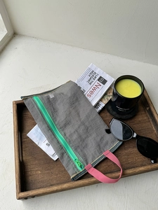 Detail of grey mesh organizer with bright green zipper and pink side handle strap