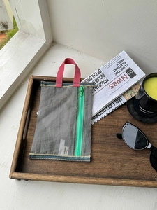 Gray mesh organizer bag with colorful trim and vibrant zipper on a wooden tray