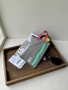 Close-up of mesh storage bag with vibrant pink handle and green zipper on wooden tray