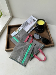 Close-up of two grey mesh organizers with green zippers and pink handles on a wooden tray