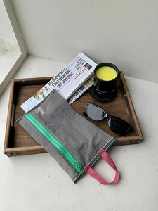 Detailed view of grey mesh organizer bag with green zipper and pink strap in a tray