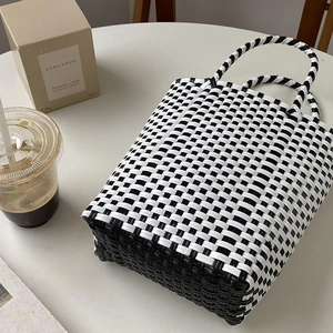 Detail of hand-woven black and white checkered tote bag with round handles on table