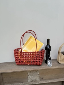 Dettaglio borsa a cesto intrecciata rossa con doppi manici su un tavolo di legno vintage