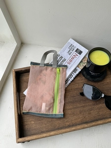 Close-up of pink mesh makeup bag with green zipper and grey handle on wooden tray