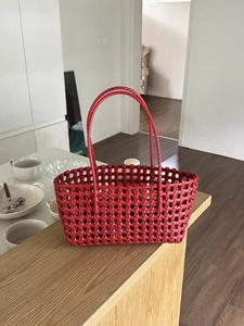 Dettaglio della borsa a cesto intrecciata rossa con design traforato e manici sottili su legno