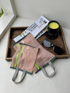 Close-up of pink mesh storage bags with neon green zippers on a wooden tray