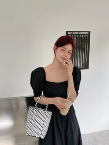 Close-up of black and white checkered woven handbag paired with a chic puff sleeve dress