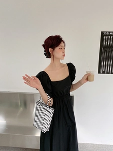 Detailed view of a black square neck puff sleeve dress paired with a woven tote bag