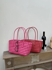 Dettaglio di borse tote intrecciate in rosa e rosso su uno scaffale in legno vintage