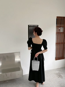 Detail view of a black and white checkerboard woven handbag paired with a retro puff sleeve dress