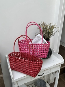 Dettaglio di borse tote intrecciate a mano in fucsia e rosso scuro su legno bianco