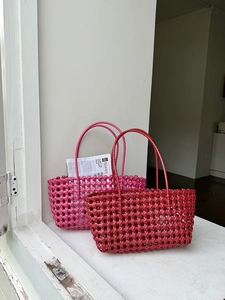 Dettaglio della borsa tote intrecciata rosa e rosso scuro su un davanzale bianco