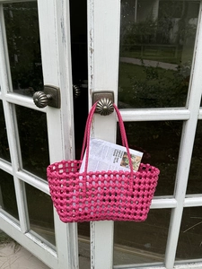 Dettaglio borsa a mano traforata rosa acceso con trama a rombi su porta in vetro bianco