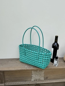 Dettaglio della borsa tote intrecciata verde acqua con trama lucida su tavolo in legno