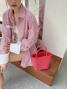 Close-up of red and white woven PVC tote bag paired with striped casual summer shirt