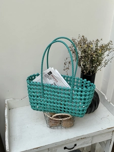Dettaglio della borsa a mano intrecciata verde pavone con motivo a rombi su tavolo rustico