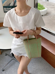 Detailed grid texture of green and orange hand-woven PVC beach tote bag held by a model