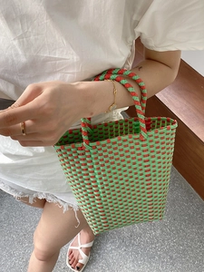 Top view of a large green and red woven PVC tote bag carried by a model outdoors