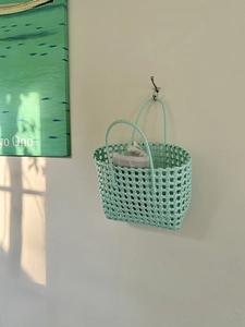 Dettaglio di una borsa a cesto intrecciata verde menta con manici tondi in un ambiente