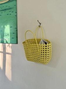 Dettaglio di borsa a cesto intrecciata gialla appesa al muro bianco con luce naturale